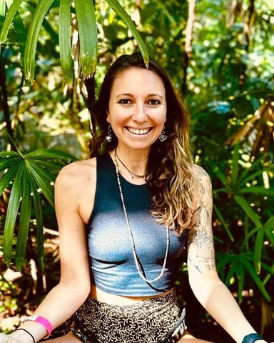 Kelsi Lehrfield, smiling, seated cross-legged among tropical greenery.